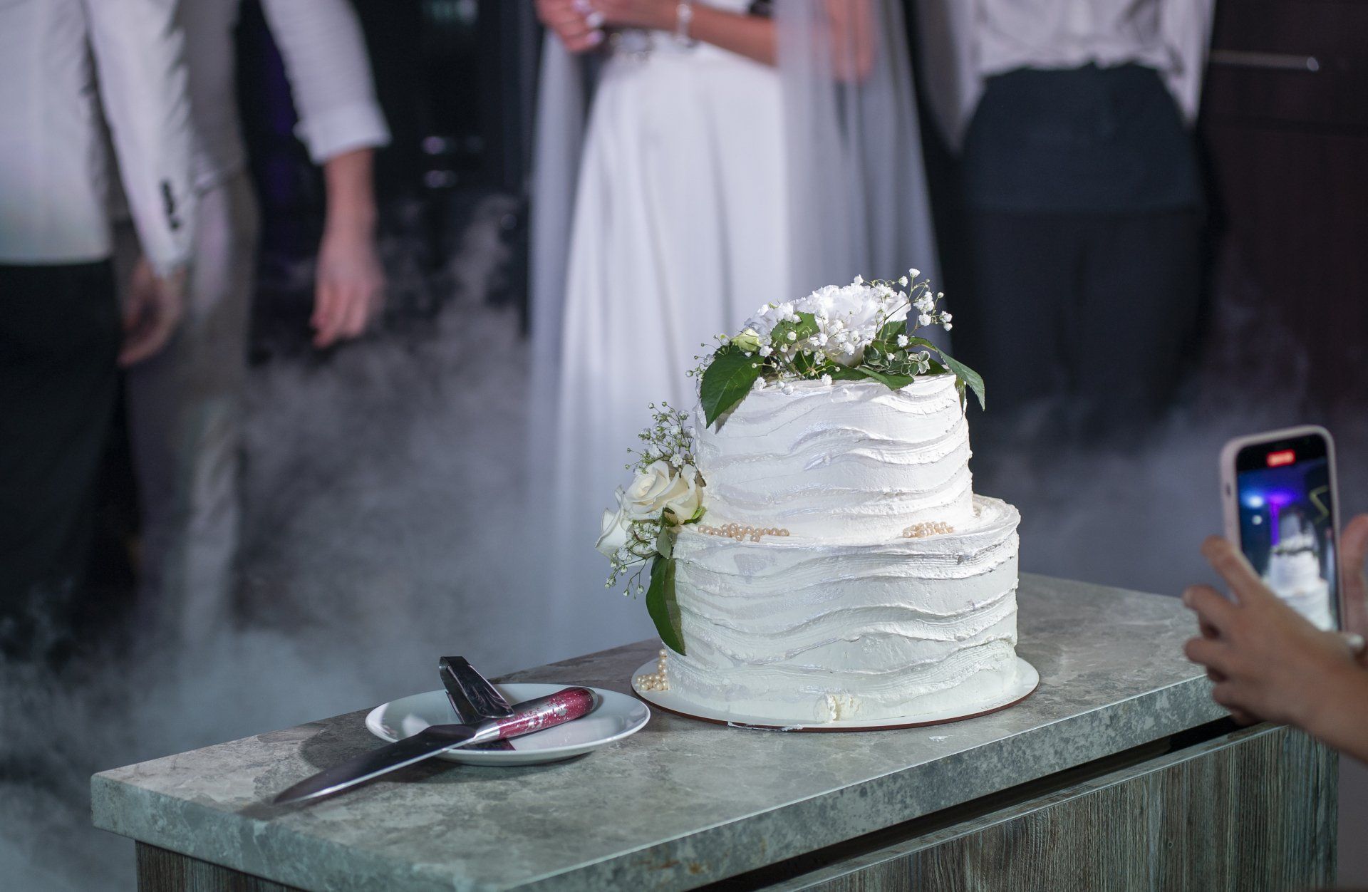A person is taking a picture of a wedding cake on a table.