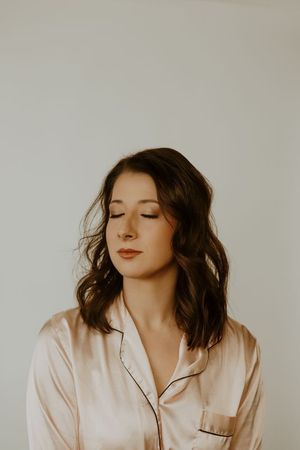 Portrait of a woman in a cream blouse, eyes closed against a plain light background