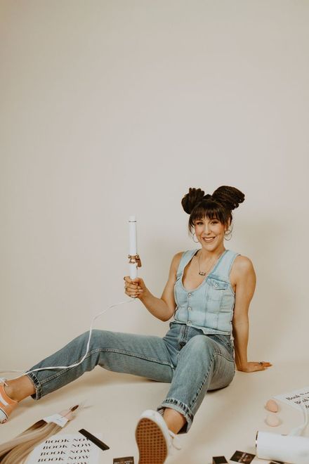 Woman sitting on the floor in a light denim outfit, holding a white candle in a minimalist room.