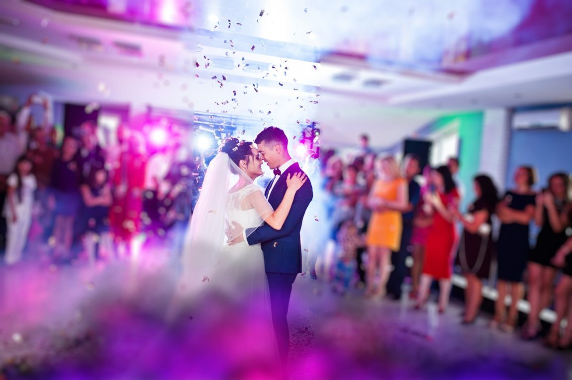 Touching and emotional first dance of the couple on their wedding with confetti and colorful lights on the background.