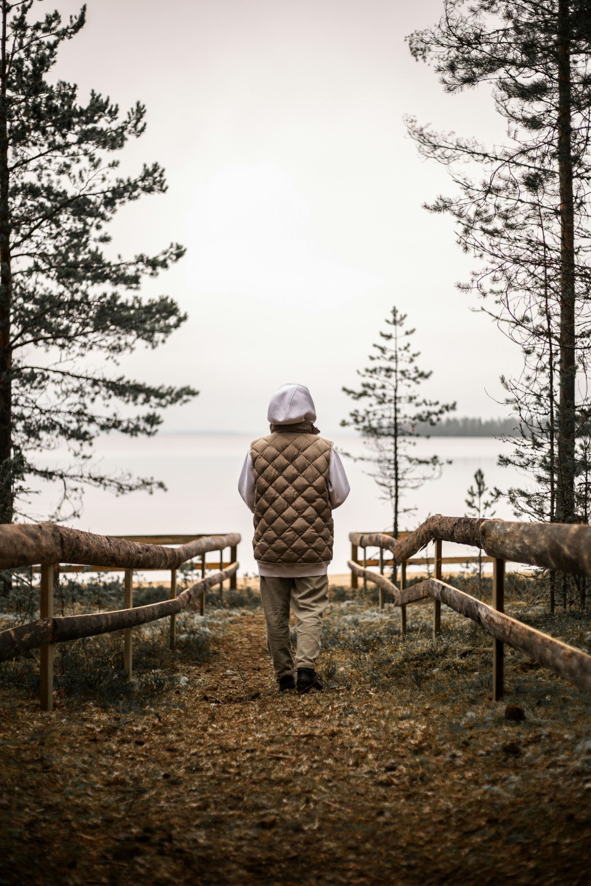 A person is walking down a path in the woods near a lake.