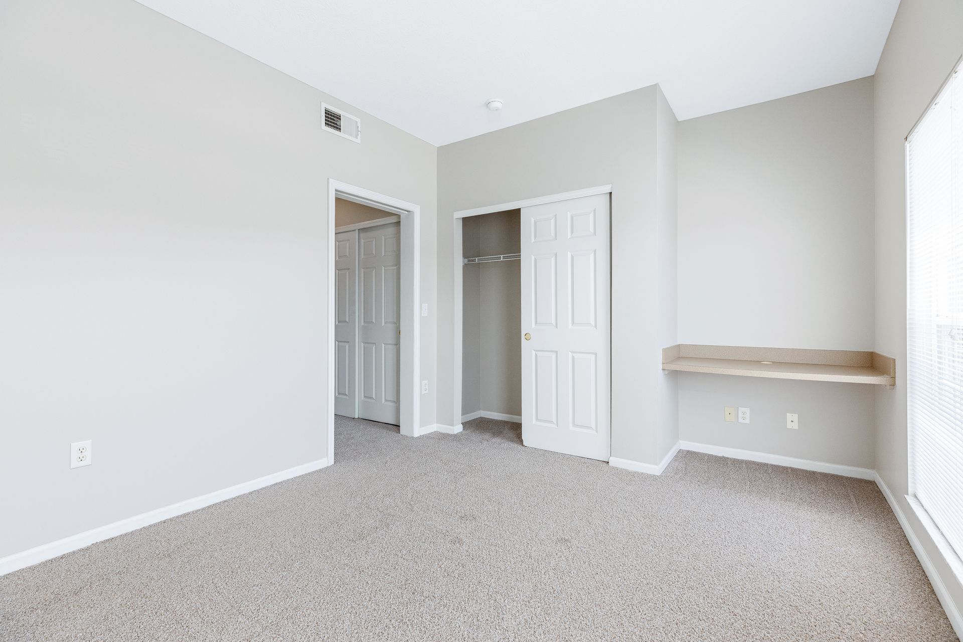 An empty bedroom with a closet and a window.