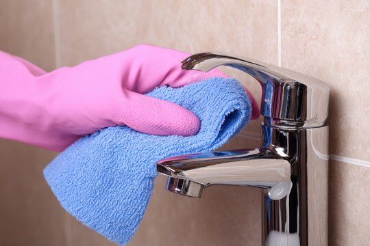 Hand in pink glove wiping chrome faucet with blue cloth.