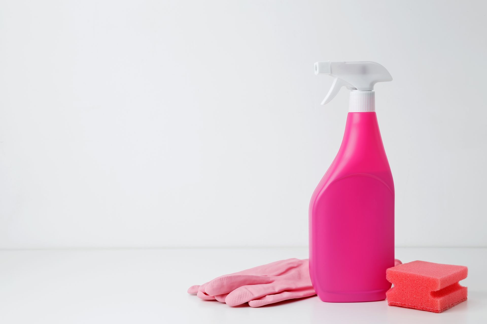 Pink spray bottle, gloves, and sponge on a white surface.