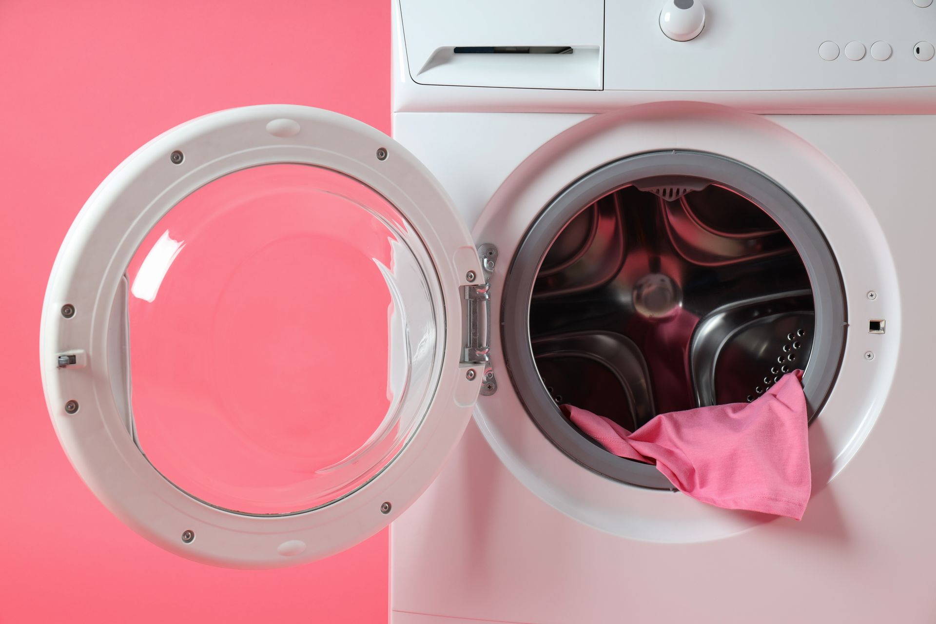 White washing machine with open door, pink fabric inside. Pink background.