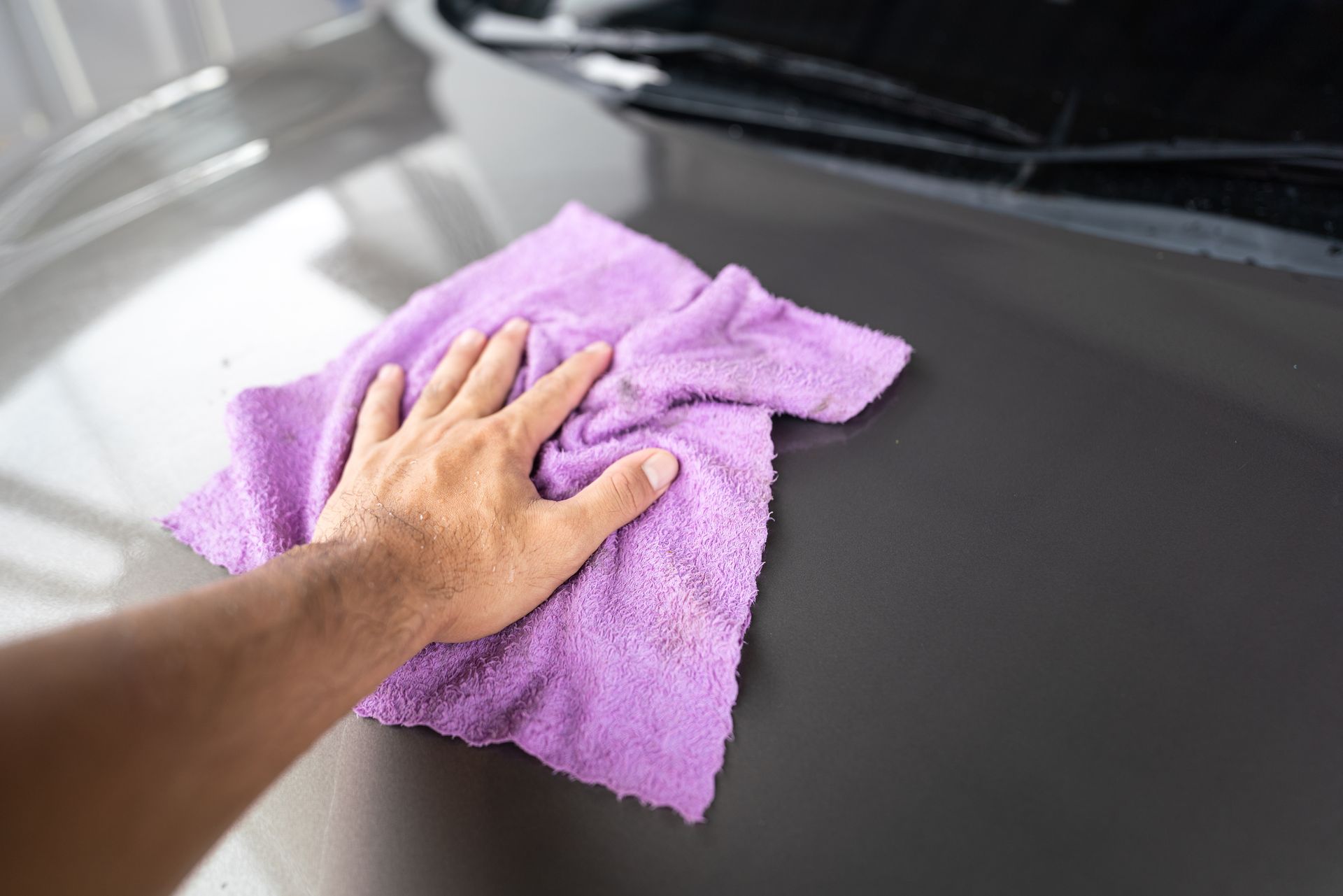 Hand wiping a purple microfiber cloth on a gray car hood.