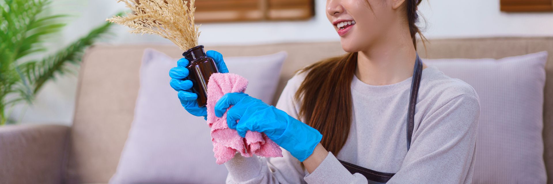Woman wearing blue gloves cleans a vase with a pink cloth; she smiles.