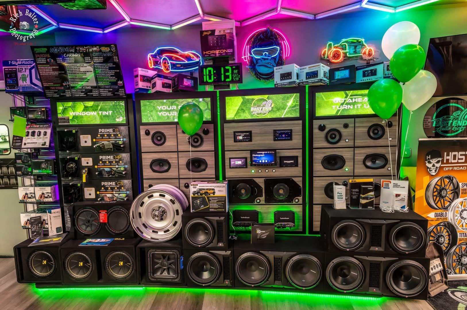 Bright room filled with stacked speakers, subwoofers, and neon green/purple LED lights | East End Auto Kicks