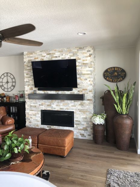 Modern living room with green sofa, fireplace, large wall TV, and wooden chairs near bright windows.