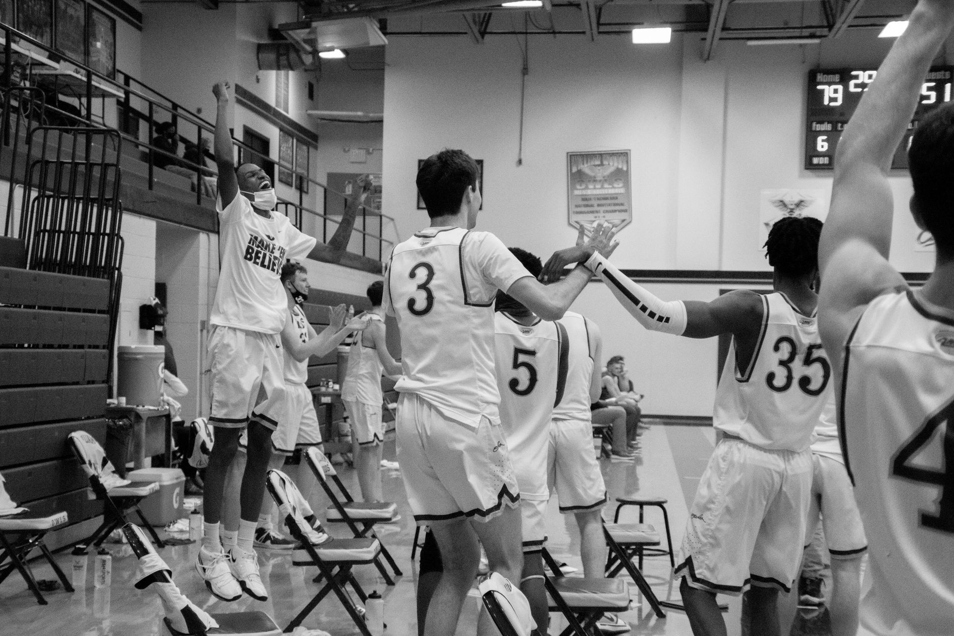 Basketball players high-five on the bench during a game in a gymnasium.