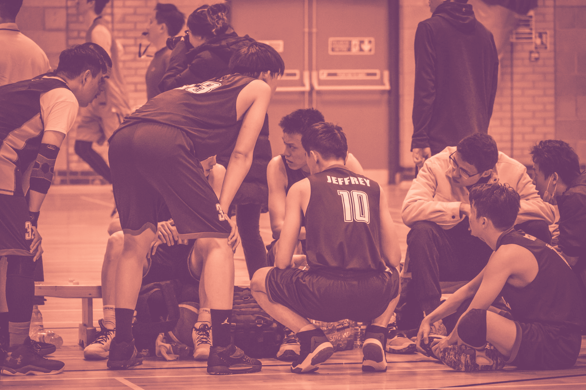 Basketball players and coach huddle during a timeout on an indoor court
