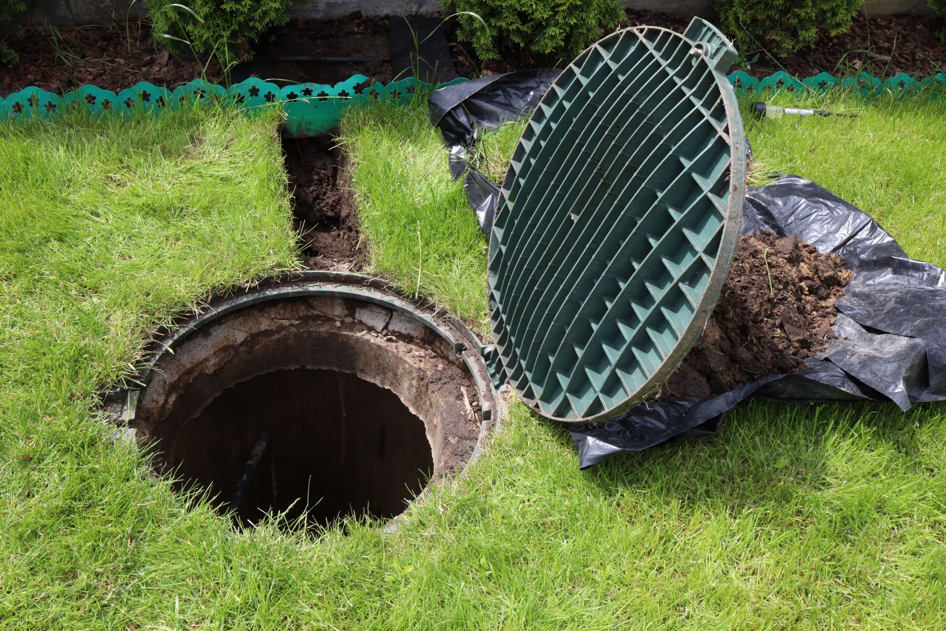 Open manhole in grass with its round metal cover leaning beside it