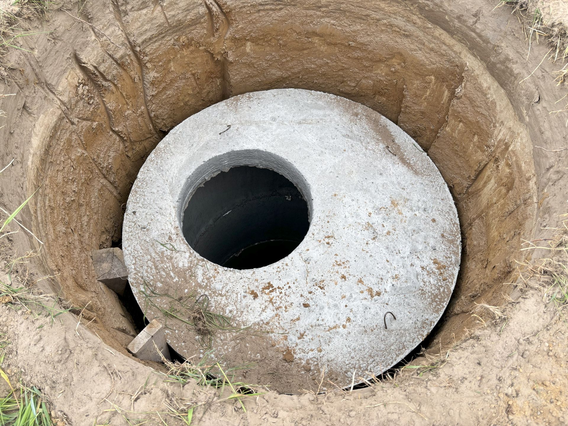 Concrete manhole cover with a large circular opening in a dirt pit