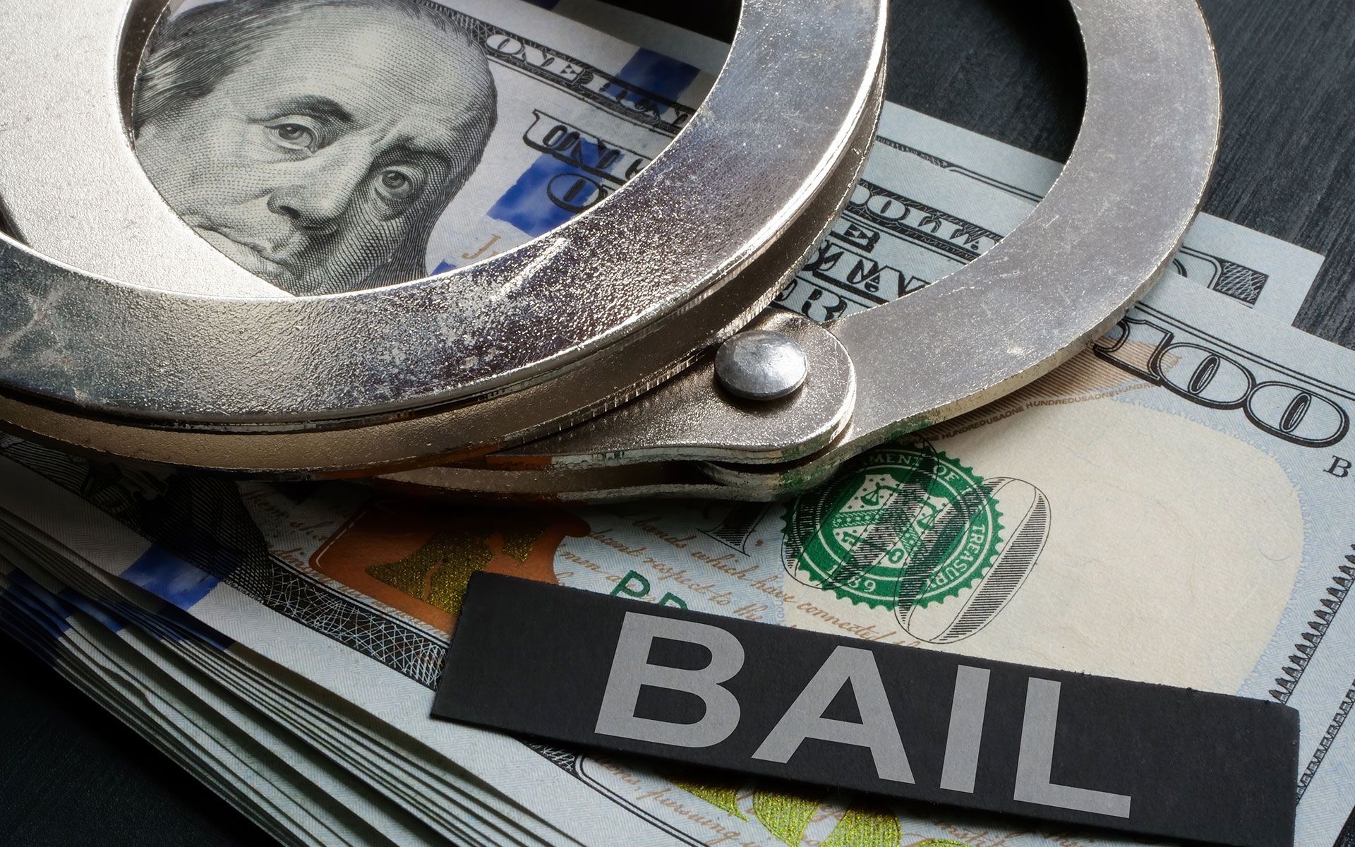 Handcuffs on a stack of US money with a black sign that reads