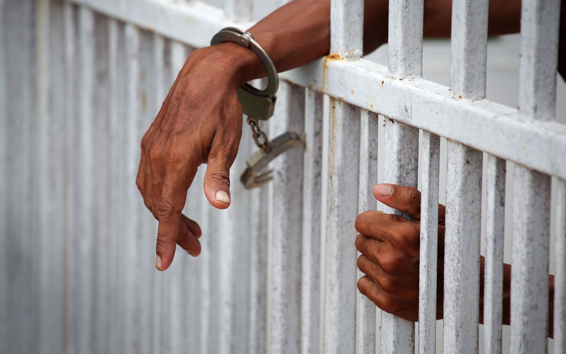 Handcuffed hands reaching through prison bars.