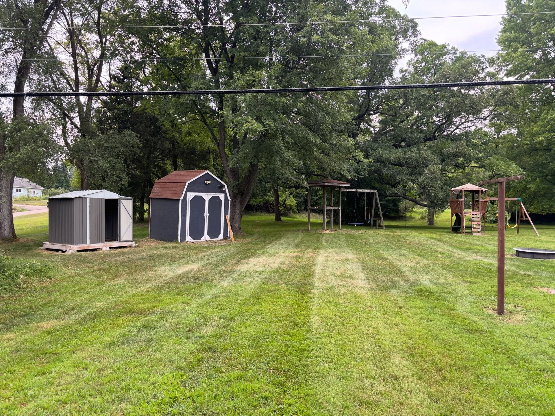 Backyard with two sheds, a tree swing, and a wooden playset on a grassy lawn