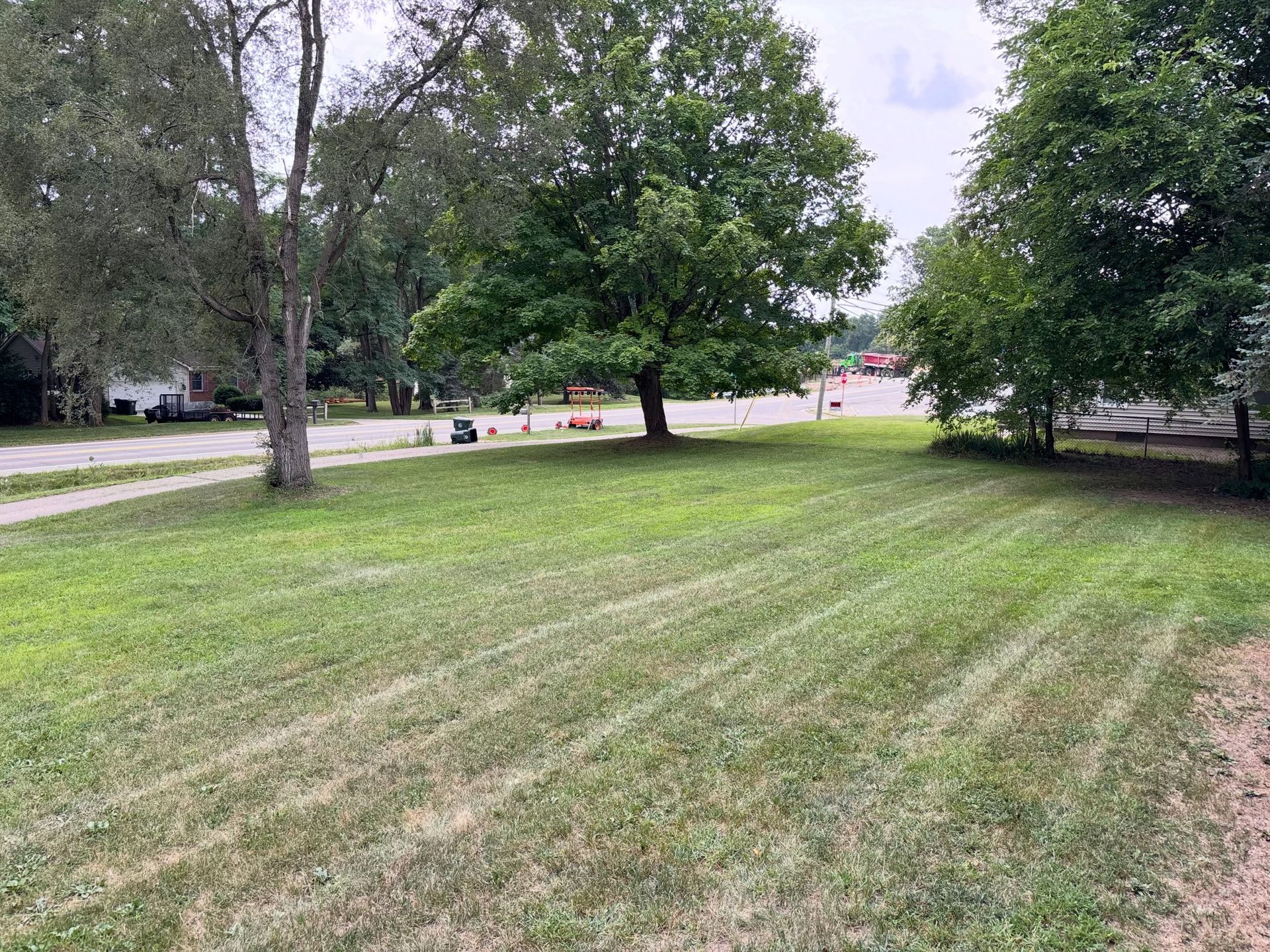 Grassy park with trees and a road in the background under a cloudy sky