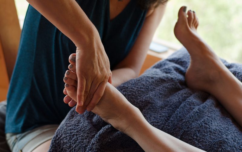 Person giving a foot massage, indoors, on a blue towel.