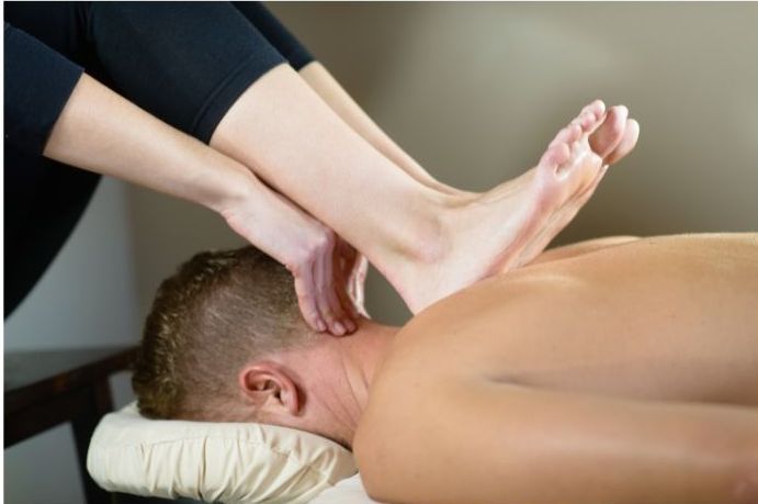 Person receiving a foot massage on the neck; therapist using foot.
