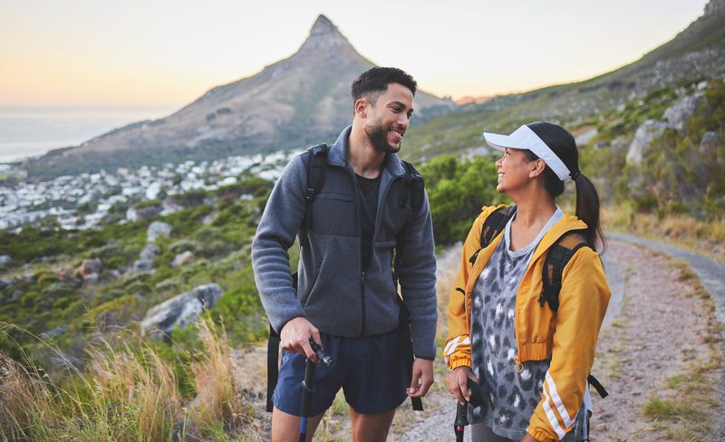 Couple hiking on a trail, looking at each other, mountain and town in background.