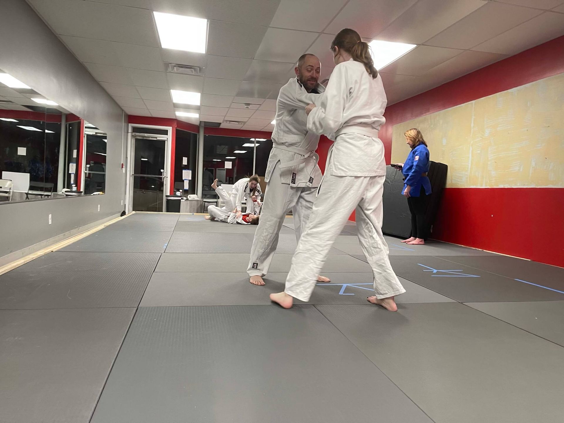 Two people practicing grappling in a martial arts studio with gray mats and red walls at Carmel Judo Indianapolis, IN