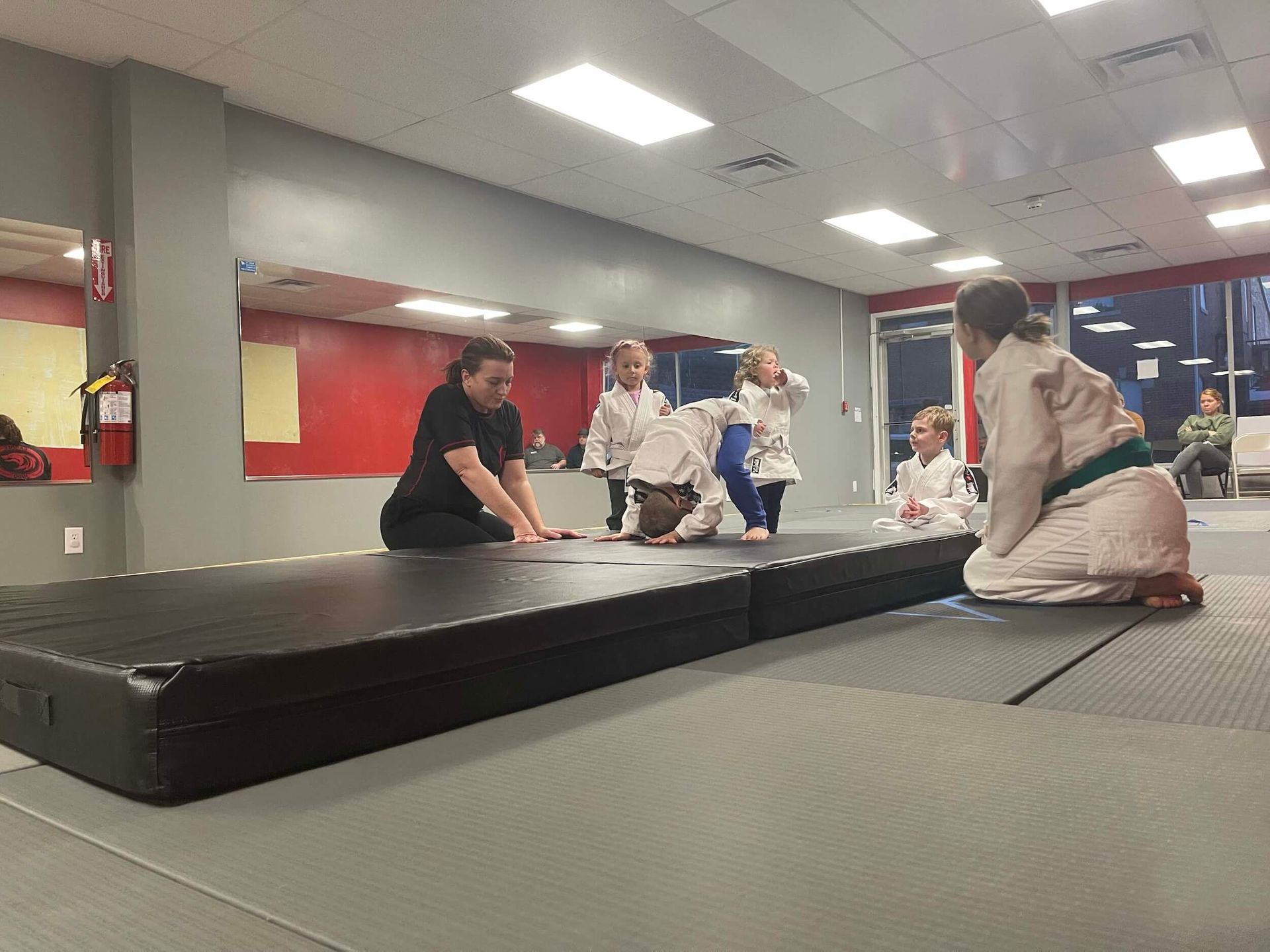 People in a martial arts studio gathered around a black mat during training at Carmel Judo Indianapolis, IN