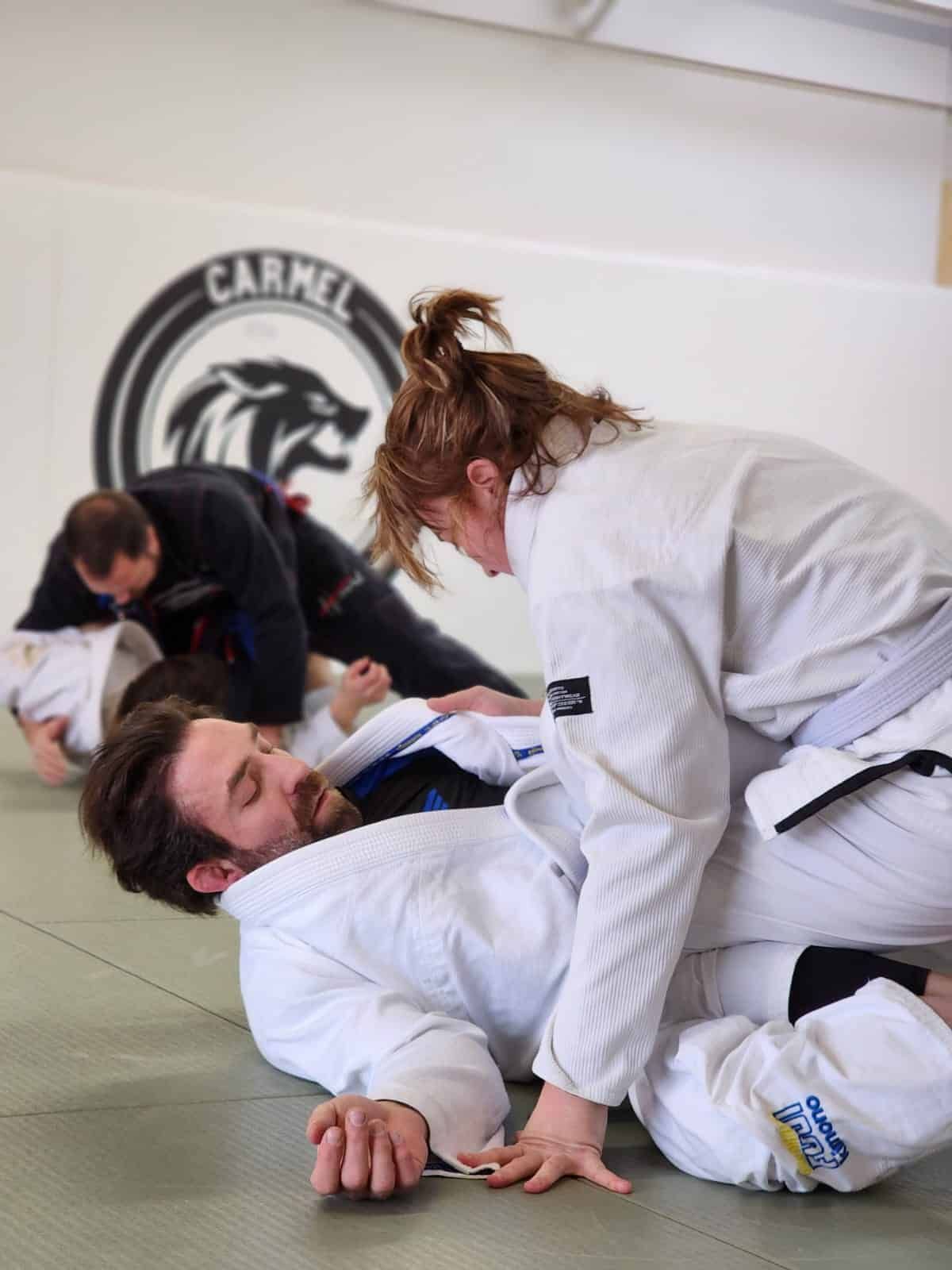 Two jiu-jitsu athletes grapple on a mat in a gym, wearing white gis and black belts at Carmel Judo Indianapolis, IN
