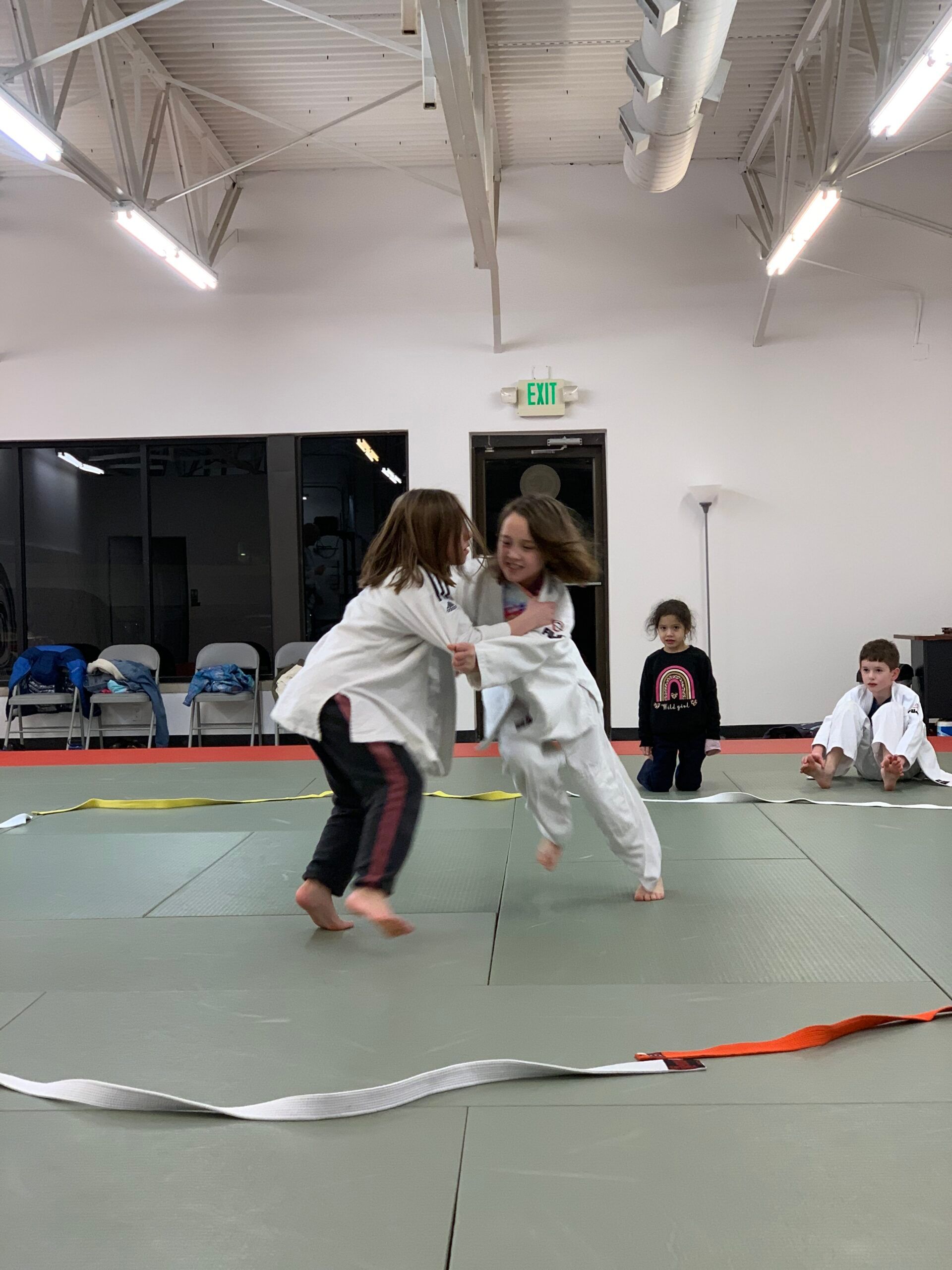 Two children sparring in martial arts uniforms on a mat in a gymnasium at Carmel Judo Indianapolis, IN
