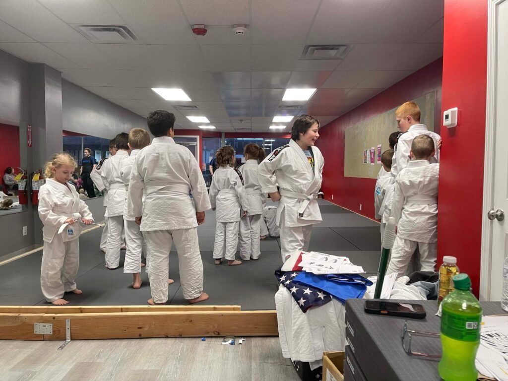 People in white clothing gathered in a dance studio with mirrors and gray walls at Carmel Judo Indianapolis, IN
