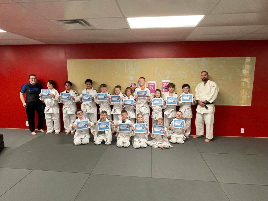 Martial arts class posing with certificates in a red-walled room at Carmel Judo Indianapolis, IN