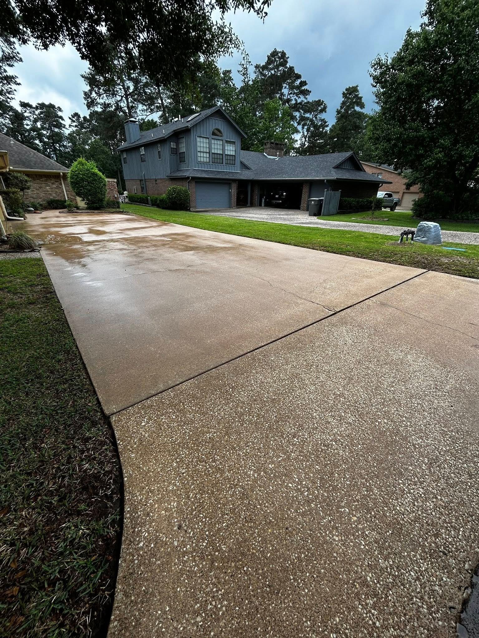 Wet driveway leading to a two-story house with a garage, under a cloudy sky.