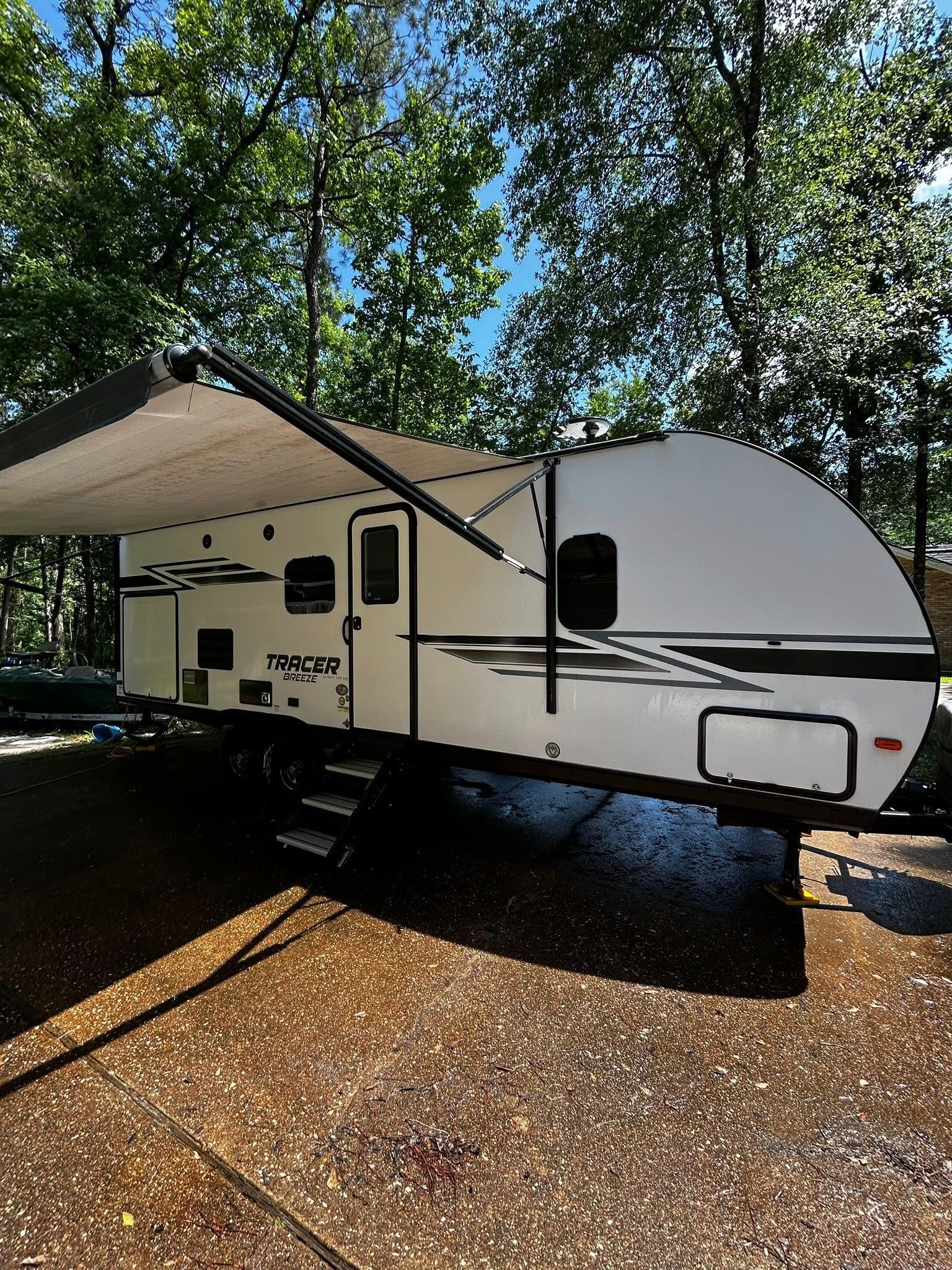 White travel trailer with awning extended, parked outdoors.