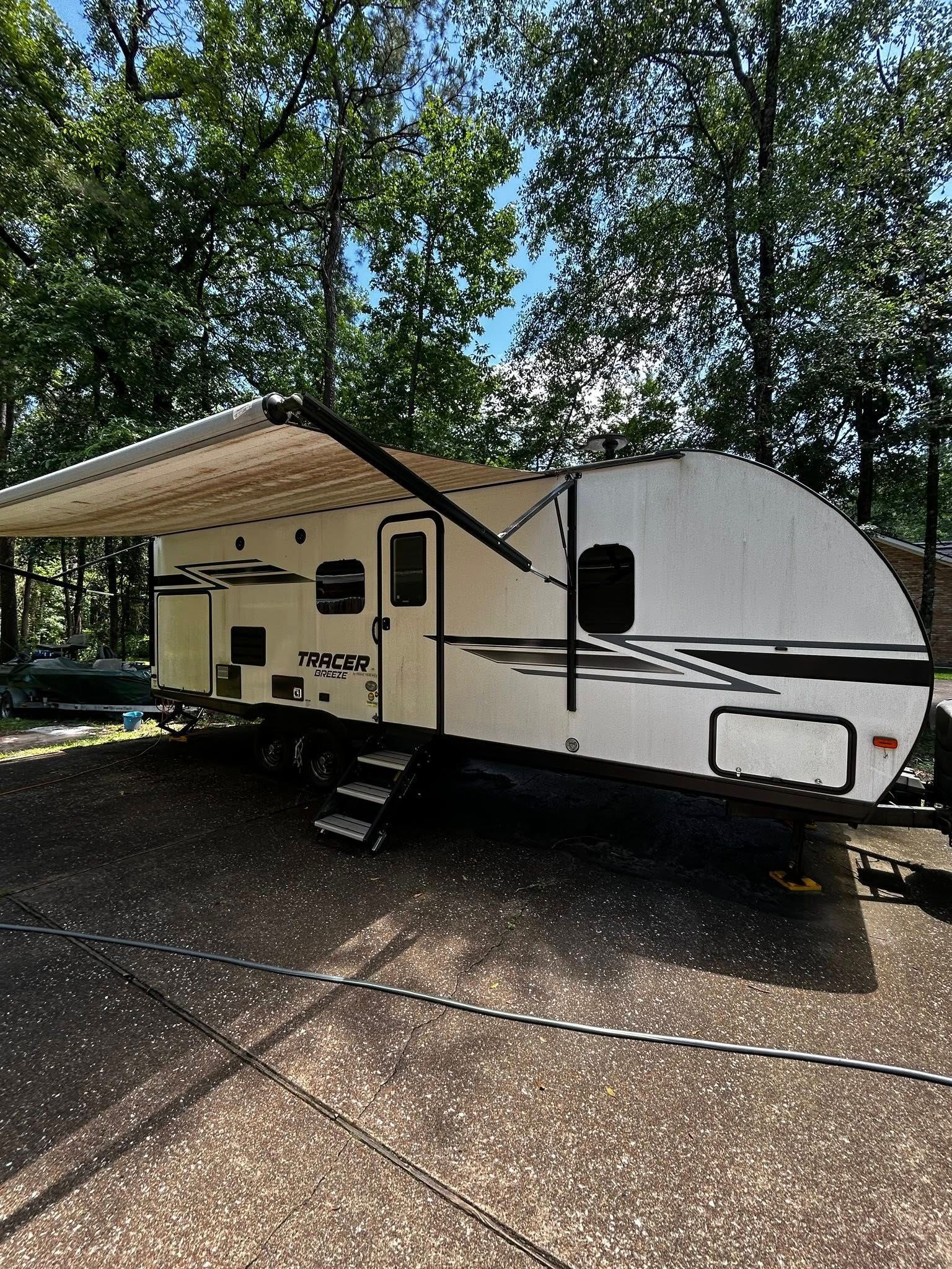 White travel trailer with awning extended, parked on gravel.