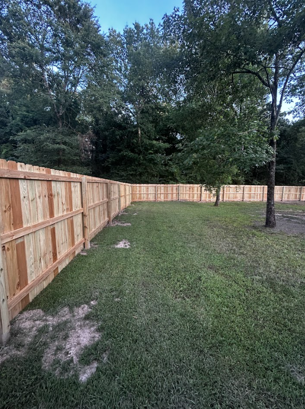 Wooden fence surrounds a grassy backyard, trees in the background.