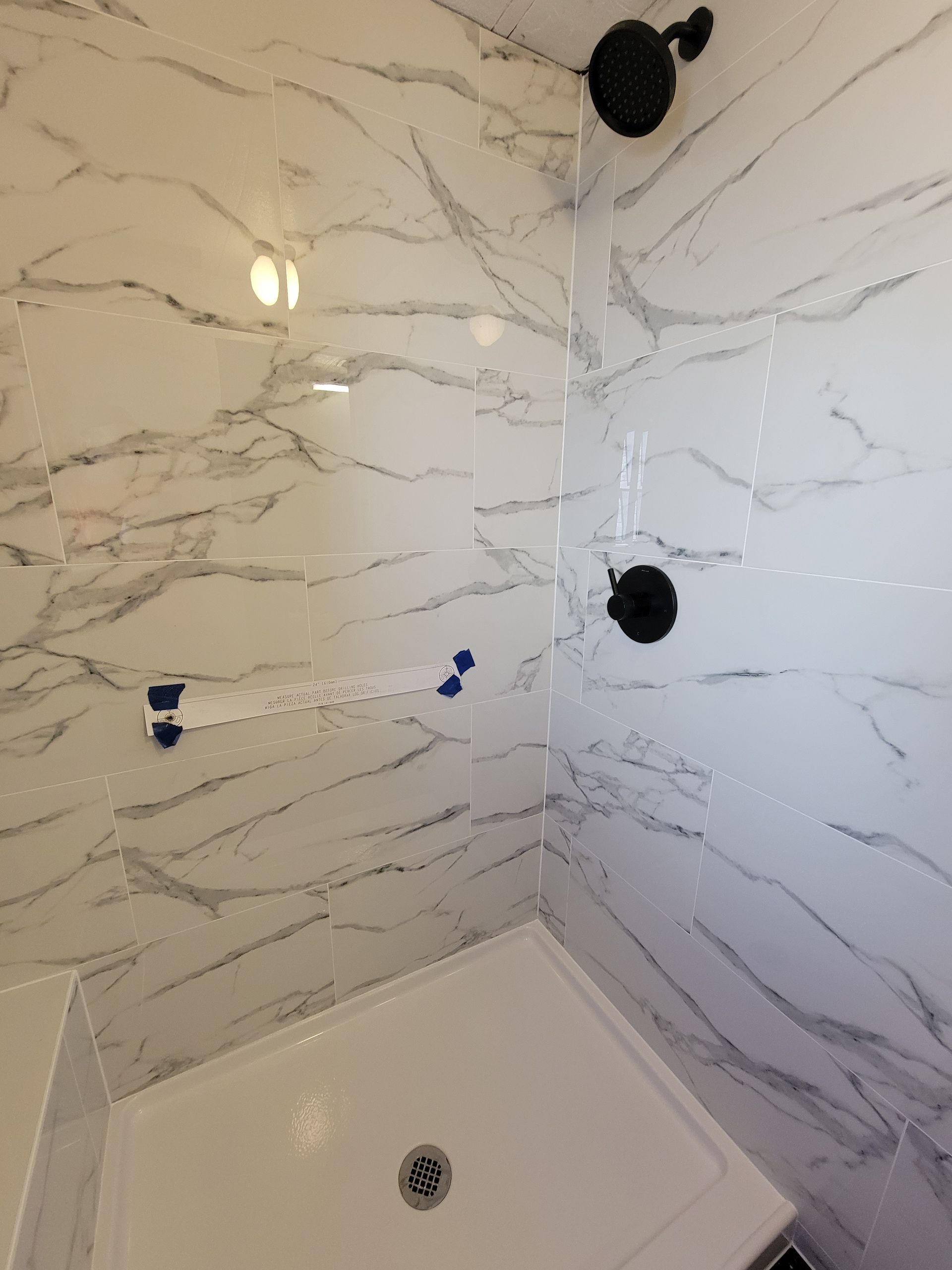 White marble-tiled shower with black fixtures and a white shower base. White marble-tiled shower with black fixtures and a white shower base.