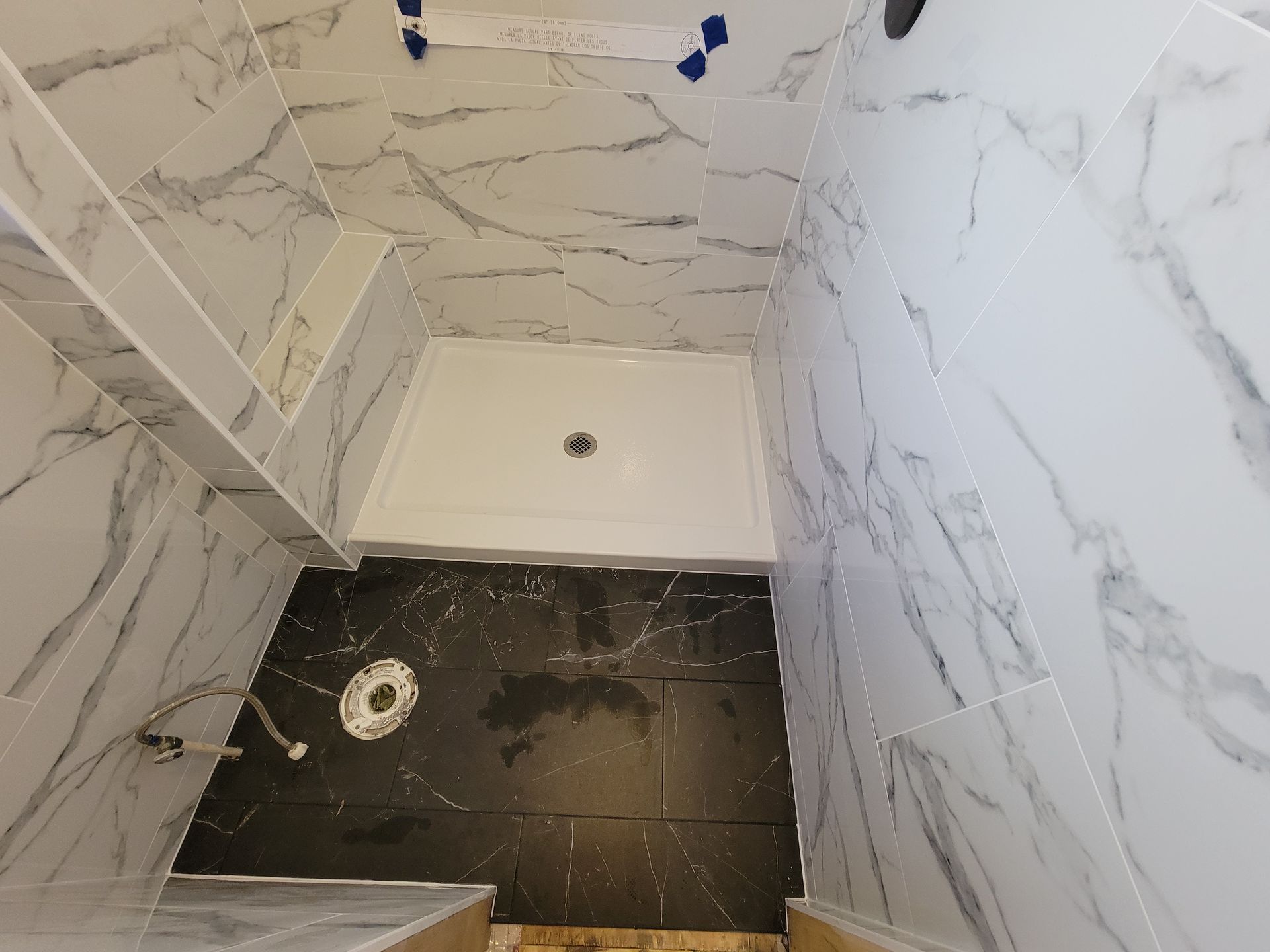 Bathroom with marble-patterned white tiles, black floor tiles, and a white shower basin. Bathroom with marble-patterned white tiles, black floor tiles, and a white shower basin.