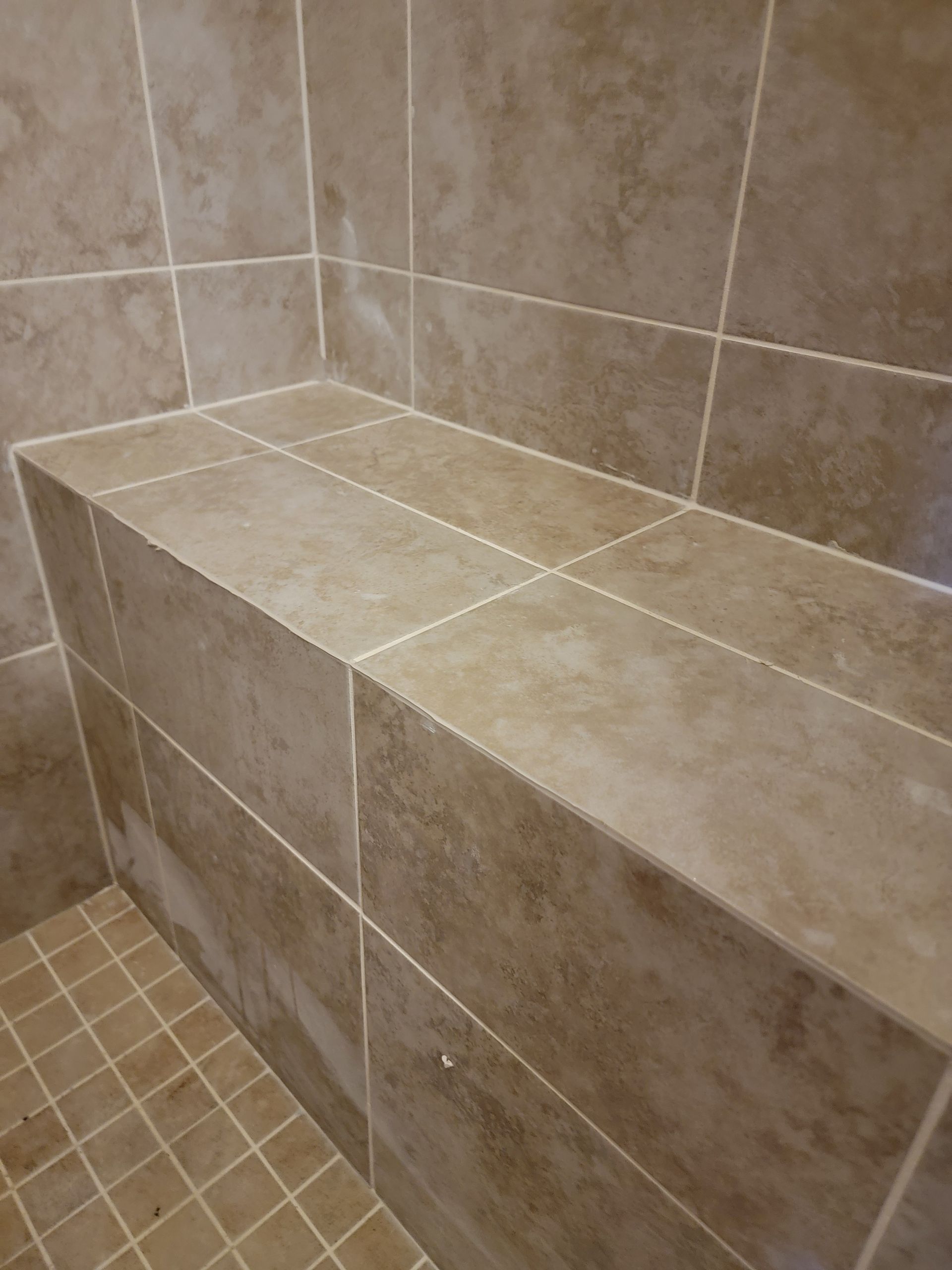 Tiled shower bench in a corner, light brown tiles. Small brown tiles on the floor. Tiled shower bench in a corner, light brown tiles. Small brown tiles on the floor.