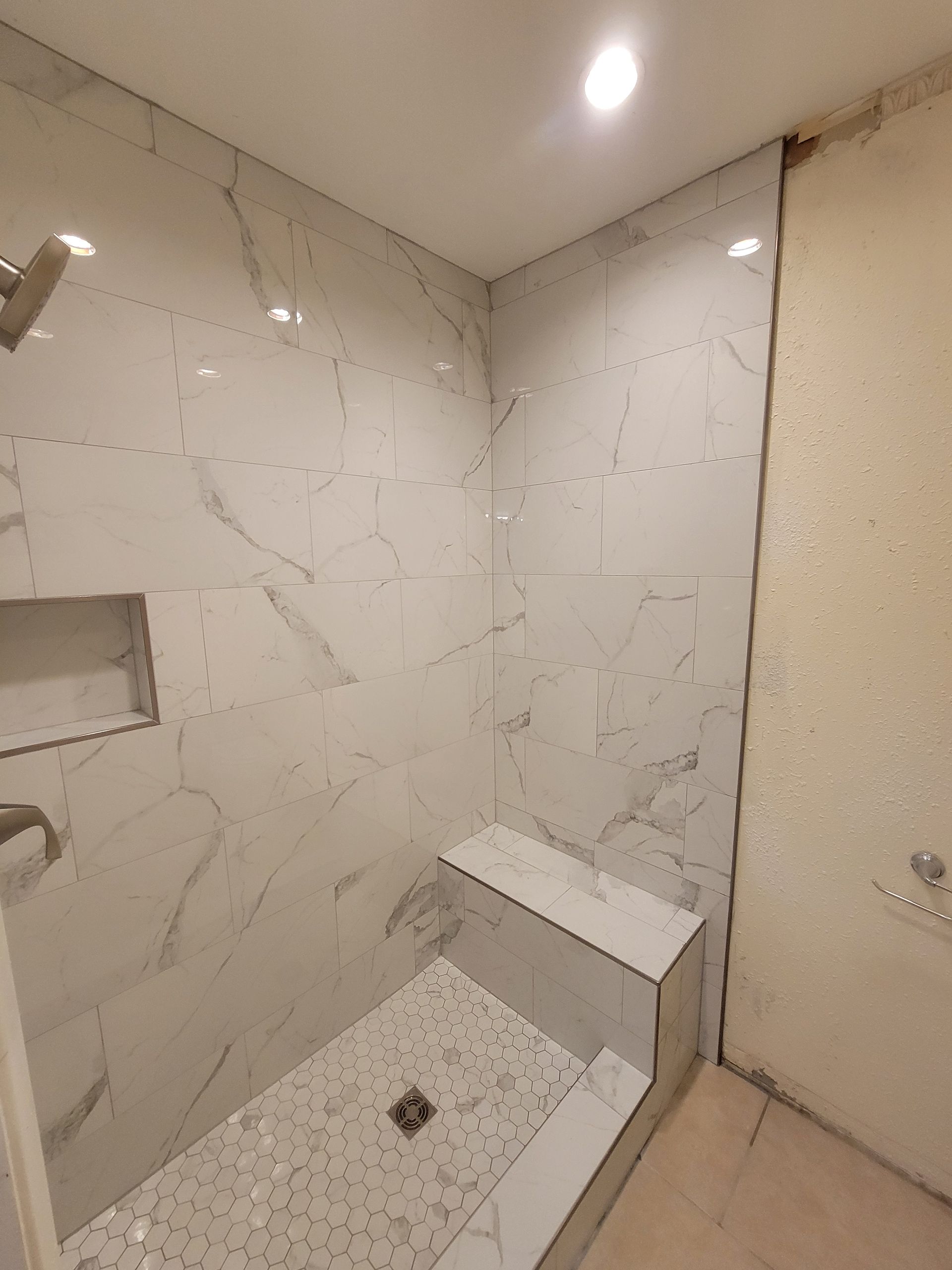 Shower stall with marble-look tiles, a built-in bench, and a recessed shelf. Shower stall with marble-look tiles, a built-in bench, and a recessed shelf.