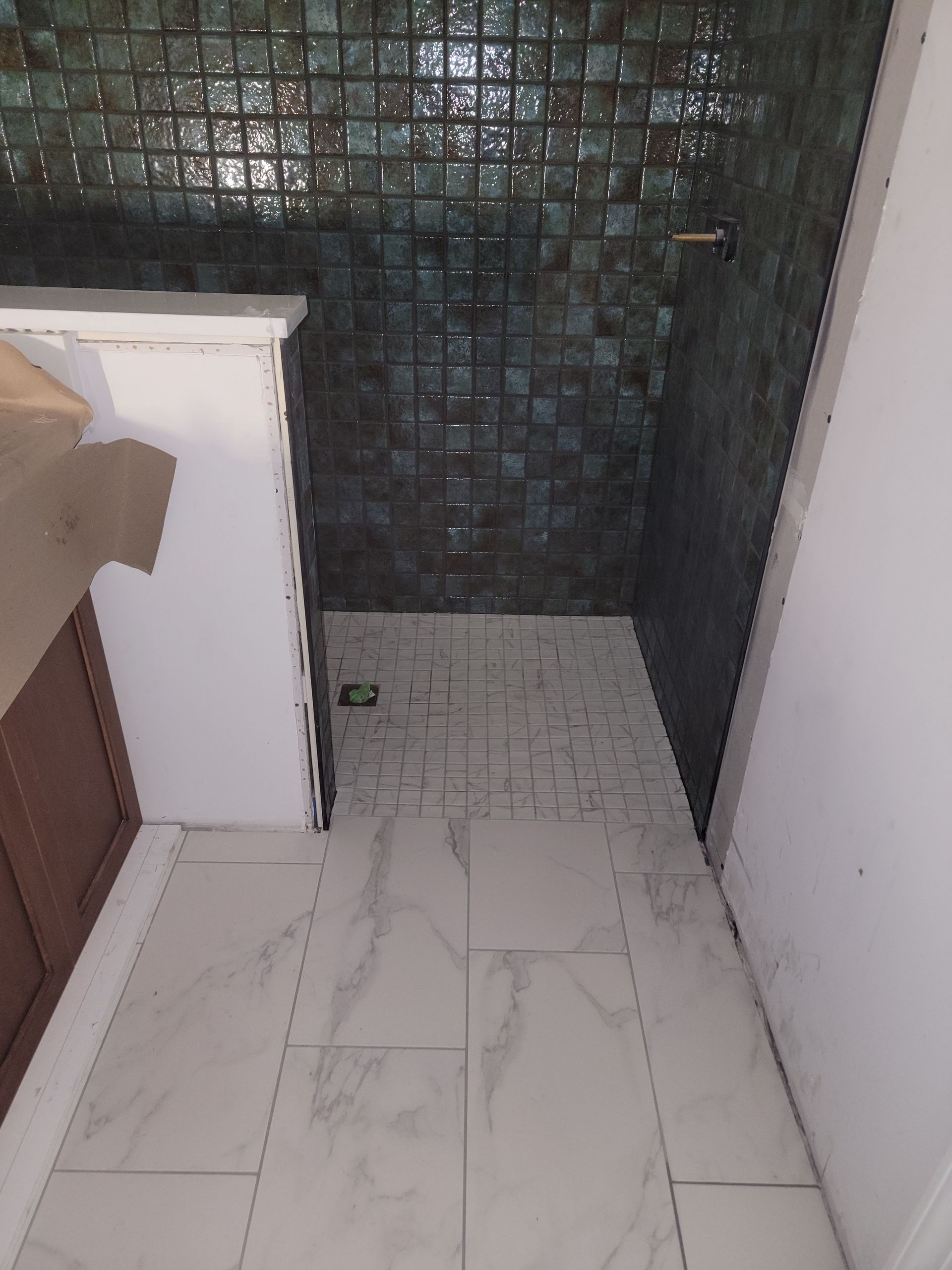 Bathroom with green tile shower wall, white floor tile, and a brown cabinet.
