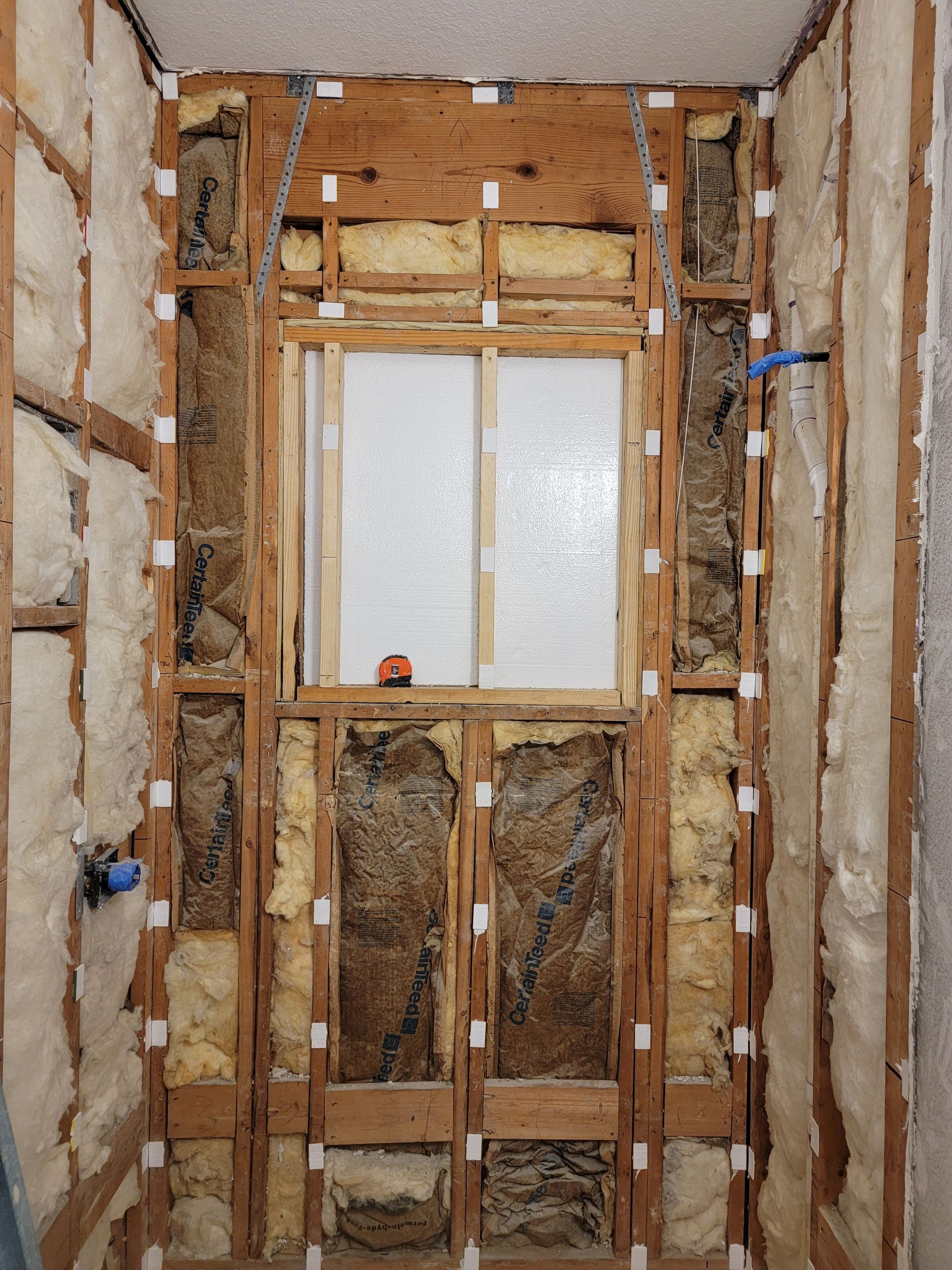 Bathroom renovation in progress, framing and insulation visible. Window centered, studs exposed, plumbing fixtures present. Bathroom renovation in progress, framing and insulation visible. Window centered, studs exposed, plumbing fixtures present.