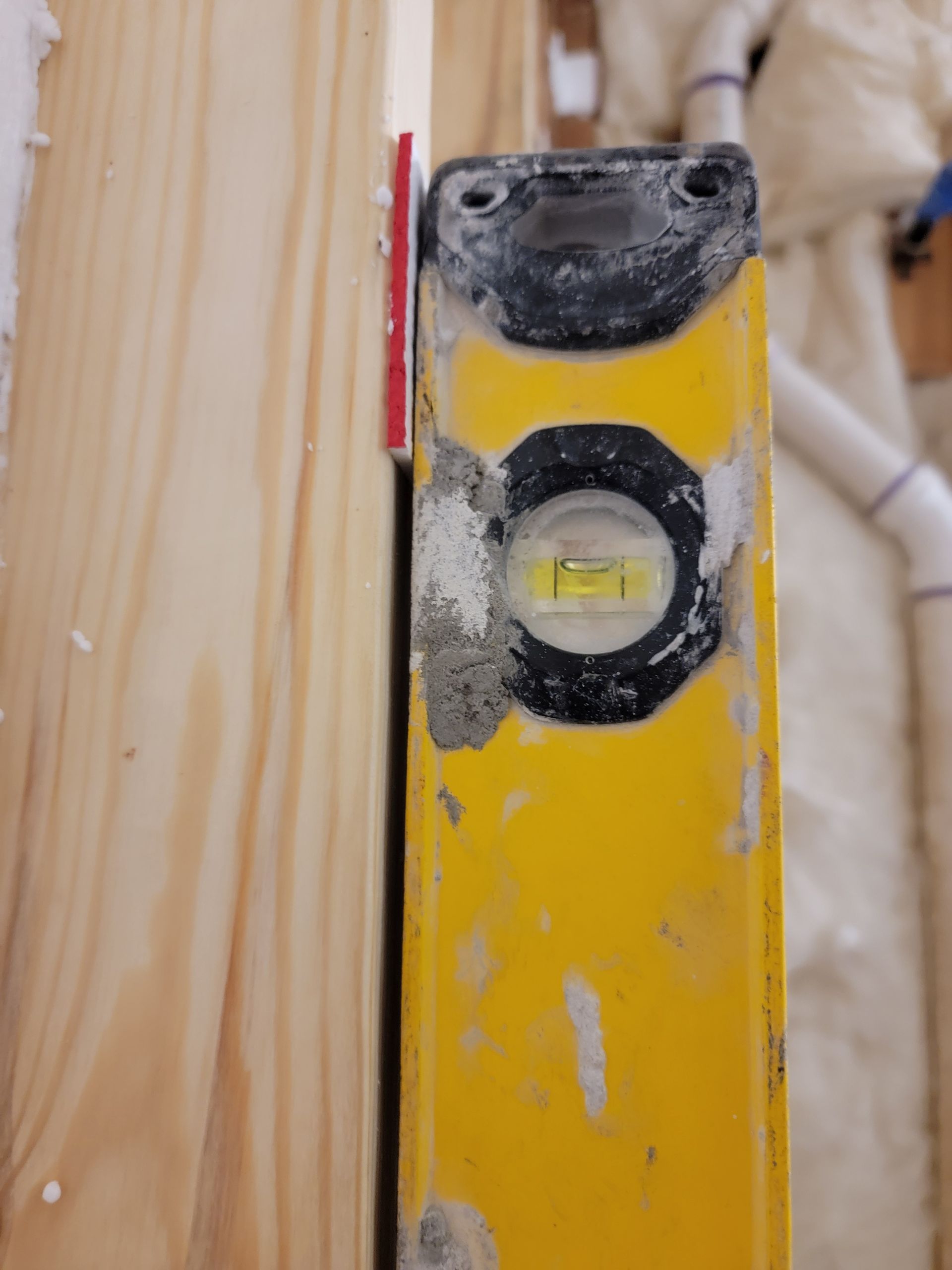 Yellow level pressed against a wooden stud with a red shim. Bubble in level is centered. Yellow level pressed against a wooden stud with a red shim. Bubble in level is centered.