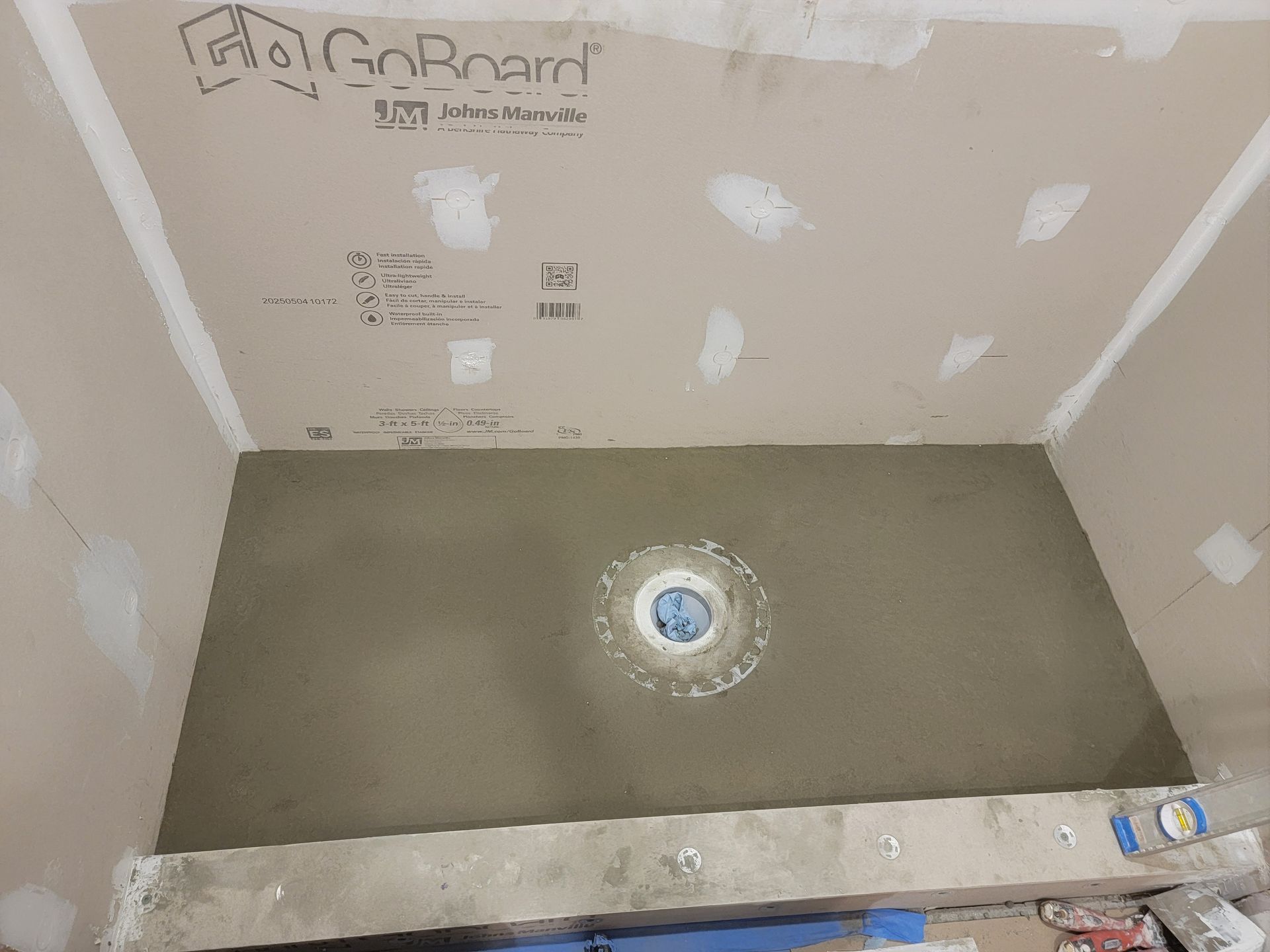 Shower construction in progress, gray cement floor with drain, light brown walls, GoBoard ceiling. Shower construction in progress, gray cement floor with drain, light brown walls, GoBoard ceiling.