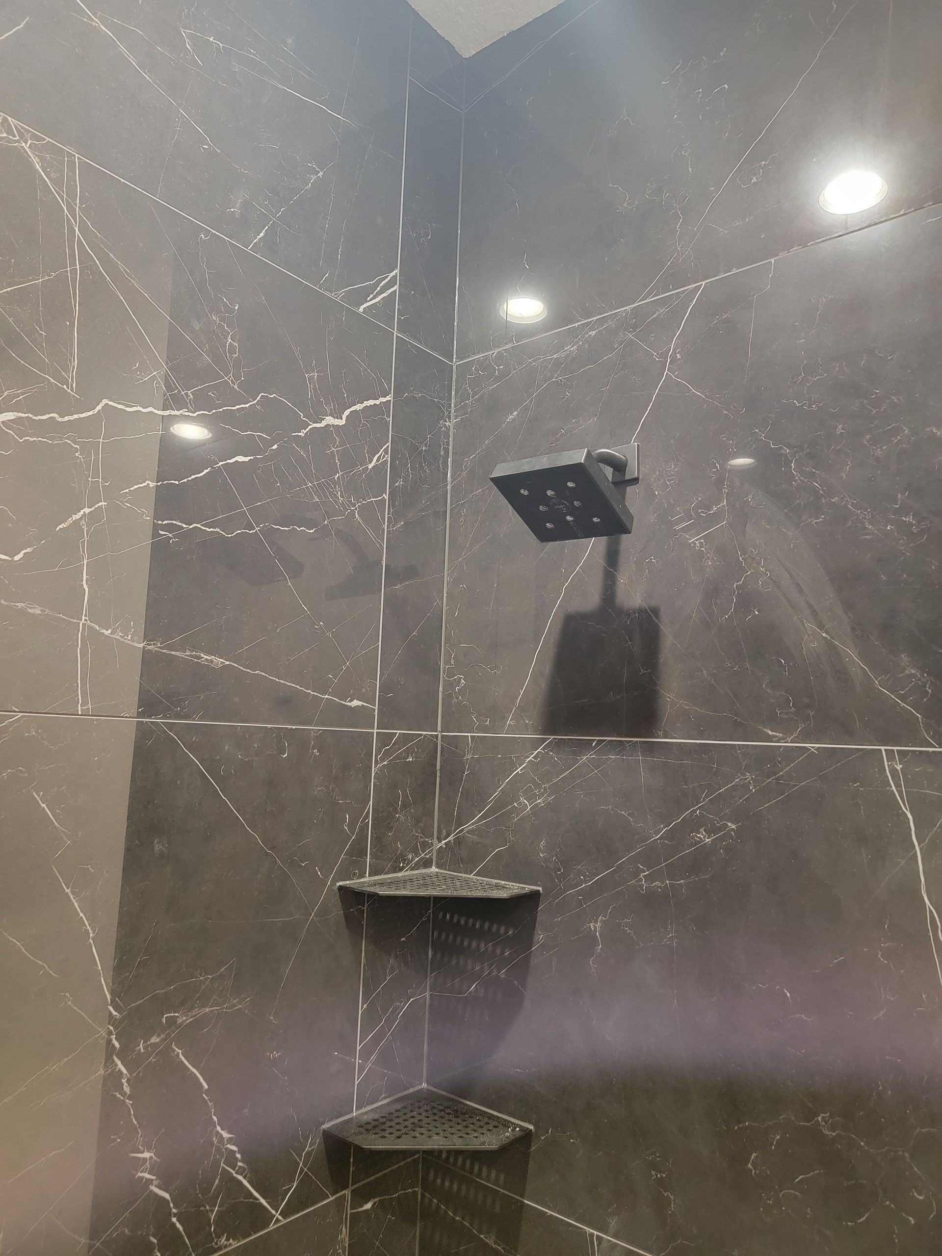 Dark tile shower with square showerhead and built-in corner shelves.