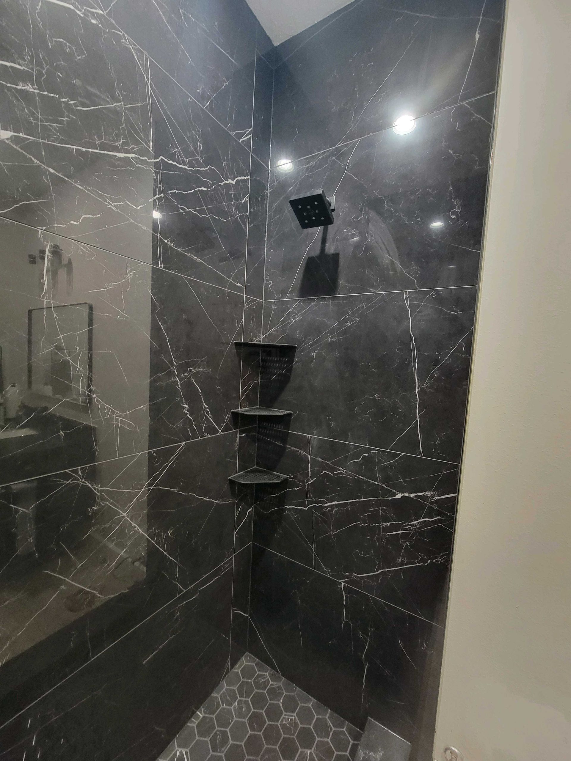 Black marble shower with hexagonal floor tiles and corner shelves. Black marble shower with hexagonal floor tiles and corner shelves.