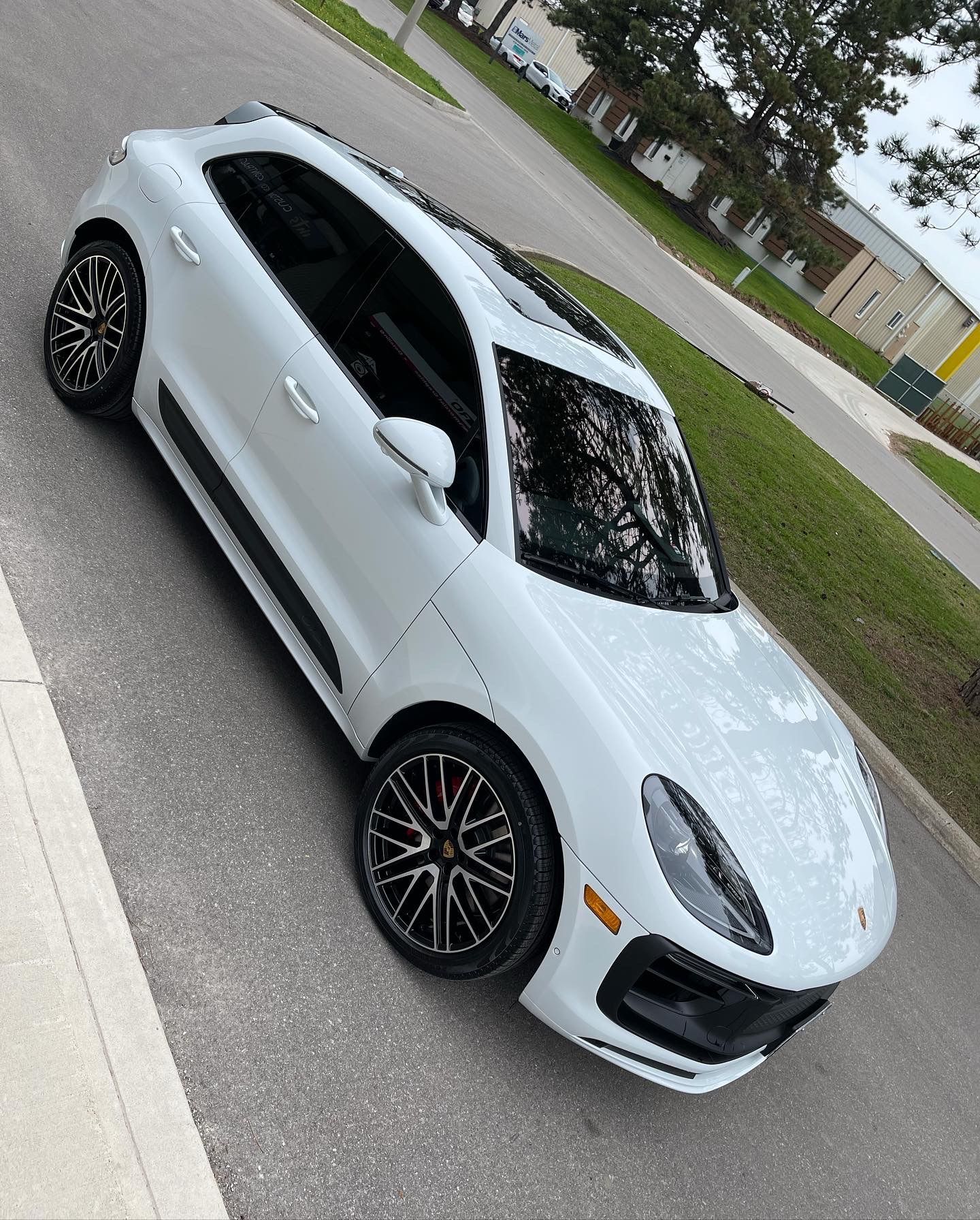 A white Porsche Macan SUV parked on an asphalt street next to a grassy area.