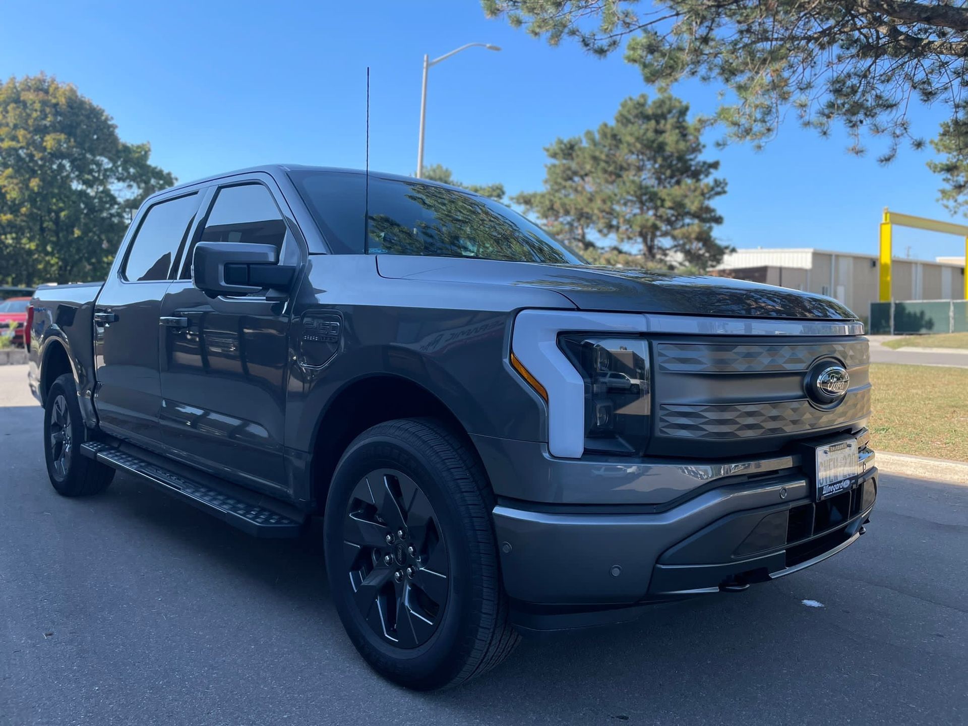A dark gray Ford F-150 Lightning electric pickup truck parked on an asphalt lot on a sunny day.