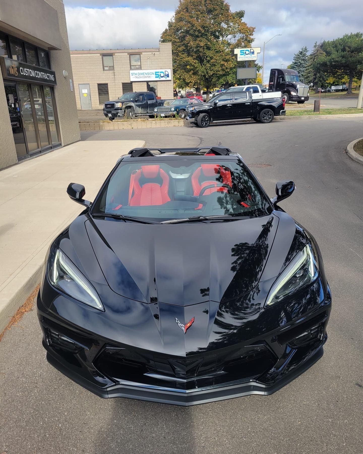 A shiny black Corvette with a bright red interior parked in a sunny outdoor lot.