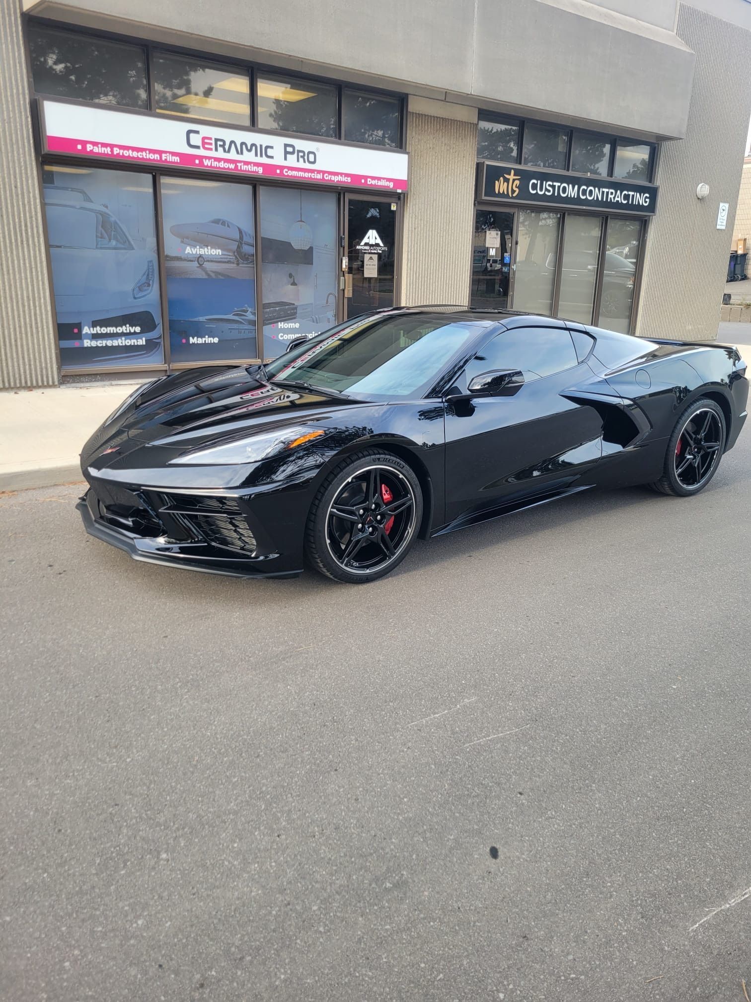 A black Chevrolet Corvette parked outside a Ceramic Pro shop storefront.