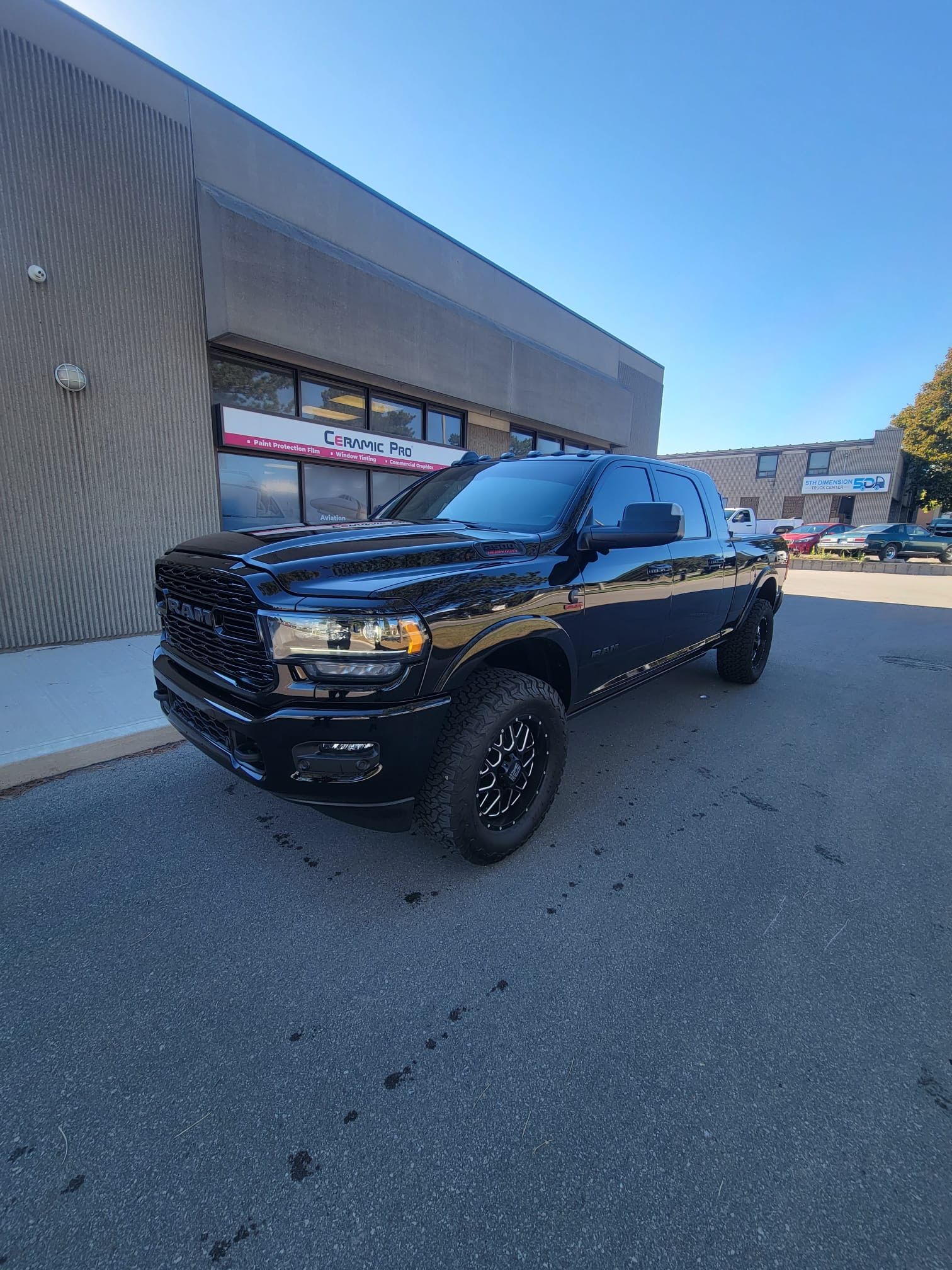A black RAM pickup truck parked in front of a commercial building on a sunny day.