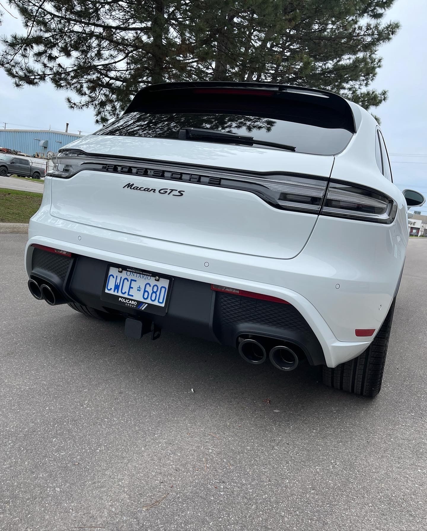 A rear view of a white Porsche Macan GTS SUV parked on asphalt with black exhaust pipes and a license plate visible.